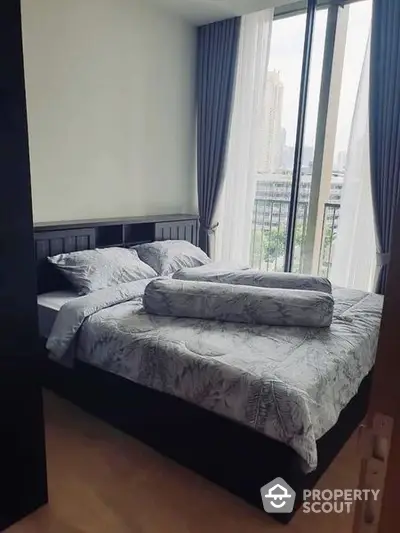 Cozy bedroom with large windows offering ample natural light and a serene city view, perfect for relaxation and comfort in a modern urban home.