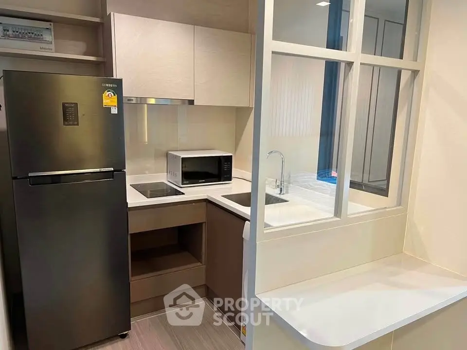 Modern kitchen with sleek appliances and open layout, featuring a fridge, microwave, and induction cooktop.