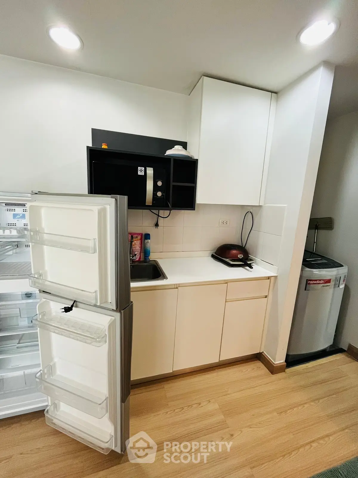 Modern compact kitchen with open fridge and washing machine, ideal for urban living.