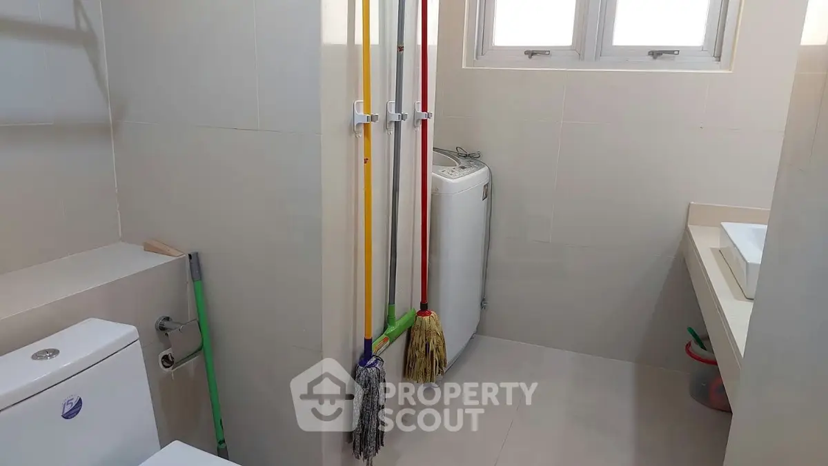 Compact bathroom with washing machine and cleaning tools, ideal for efficient space utilization.
