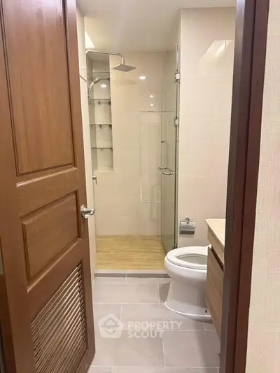 Modern bathroom with glass shower and wooden accents in a contemporary apartment.