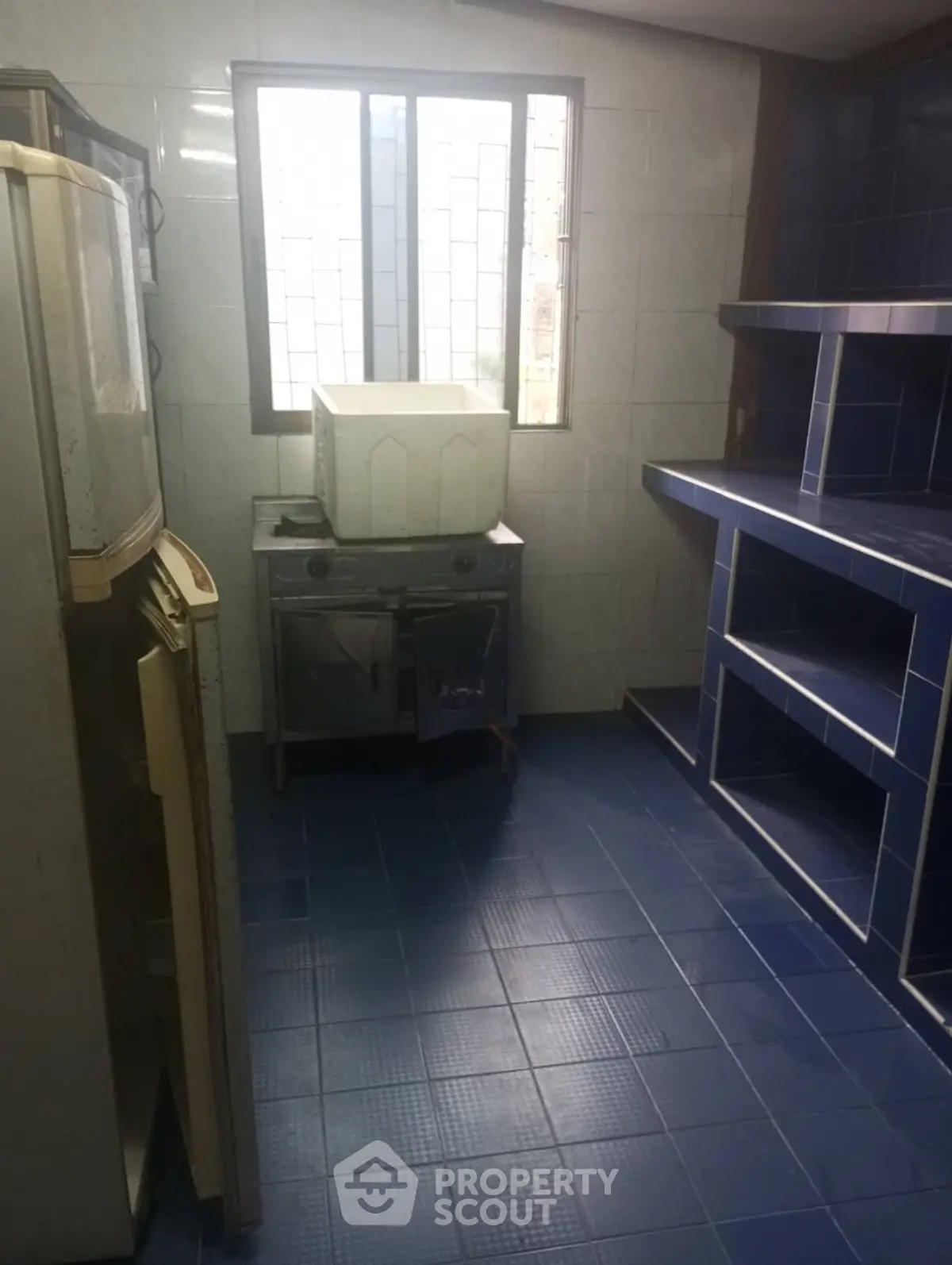Compact kitchen with blue tiled flooring and walls, featuring a small stove and refrigerator.