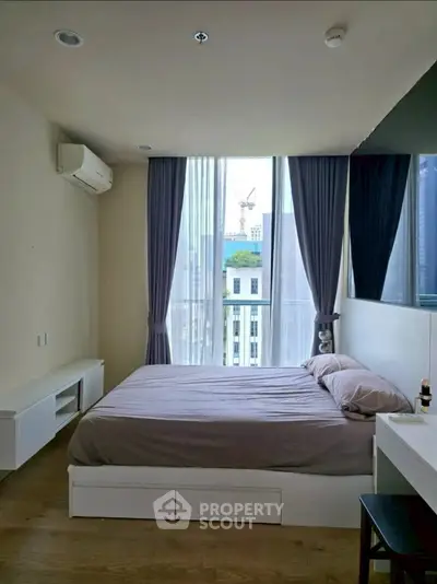 Modern bedroom with large window and city view, featuring sleek furniture and neutral tones.