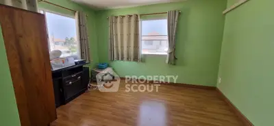Spacious room with green walls and wooden flooring, featuring large windows for natural light.