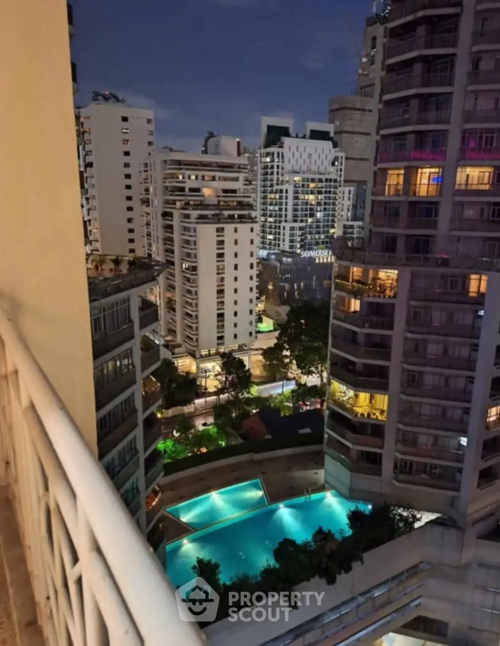 Stunning cityscape view from balcony overlooking illuminated pool and modern high-rise buildings.