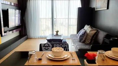 Modern living room with large TV and cozy seating area, featuring a bright window view.