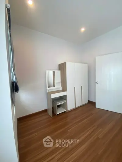 Spacious bedroom with modern wardrobe and vanity set, featuring elegant wooden flooring.