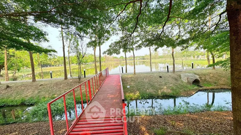 Scenic garden view with red bridge over tranquil pond, surrounded by lush greenery.