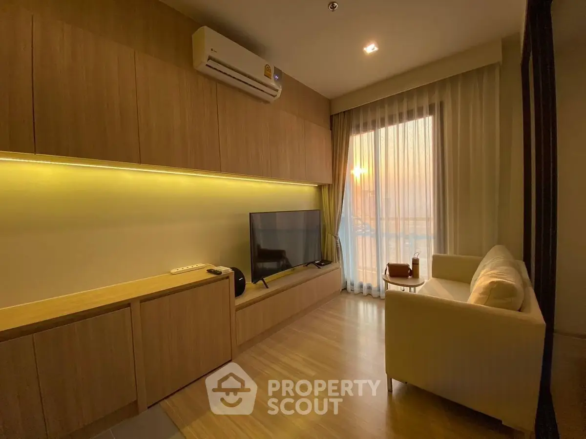 Modern living room with wooden flooring, cozy sofa, and large TV, featuring sunset view through sheer curtains.