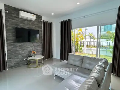 Modern living room with sleek gray sofa, wall-mounted TV, and large window overlooking garden.