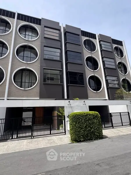 Modern apartment building with circular windows and sleek facade design.