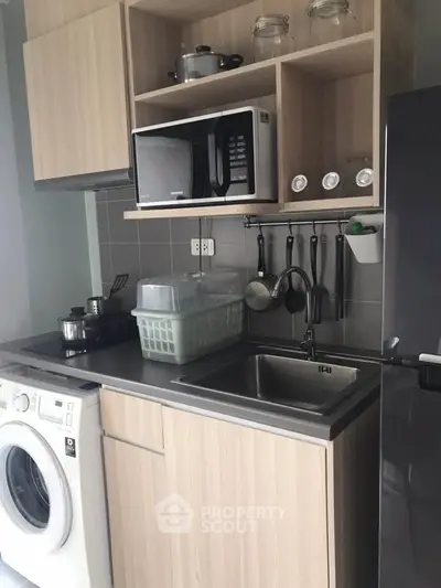 Modern compact kitchen with washing machine and microwave, ideal for urban living.