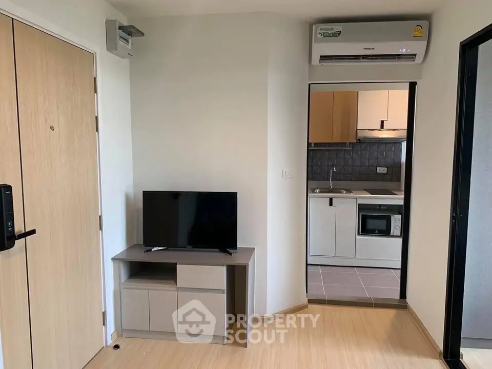 Modern apartment interior with compact kitchen and cozy living area featuring a TV and air conditioning.