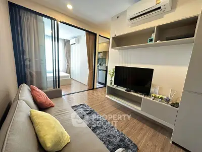 Modern living room with cozy sofa, TV, and sliding glass doors leading to a bedroom.