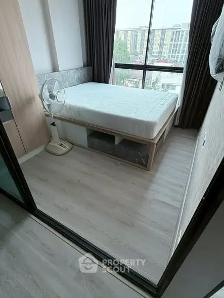 Modern bedroom with large window and city view, featuring a minimalist design and light wood flooring.