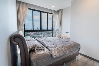 Modern bedroom with large window offering stunning city views, featuring cozy bedding and elegant curtains.