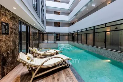 Luxurious indoor pool with elegant lounge chairs in modern apartment complex.