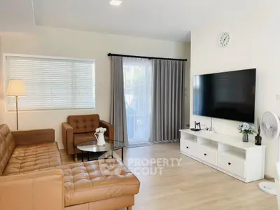 Modern living room with brown leather sofa, large TV, and natural light from window.