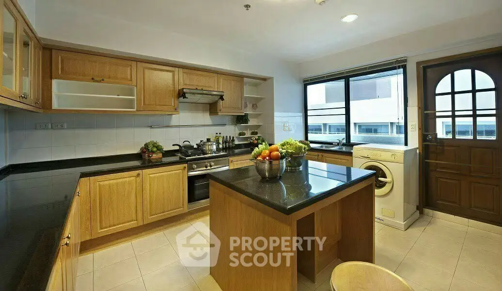 Spacious kitchen with wooden cabinets, island, and washing machine, perfect for modern living.
