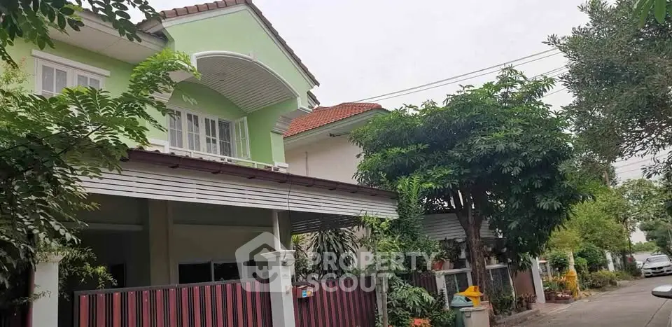 Charming two-story green house with lush garden and spacious balcony in a serene neighborhood.