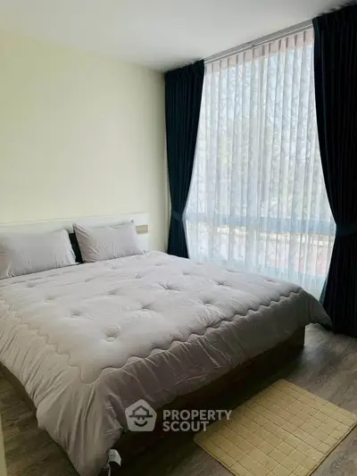 Spacious bedroom with large window and elegant curtains, featuring a cozy bed and stylish decor.