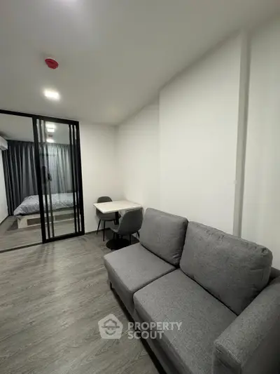 Modern apartment interior with cozy living room and bedroom separated by glass doors, featuring sleek furniture.