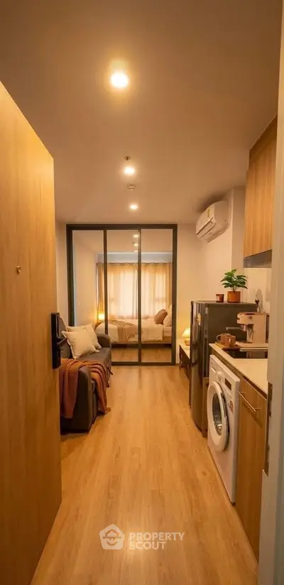 Cozy apartment entrance with wooden flooring, washing machine, and view into a warmly lit bedroom.
