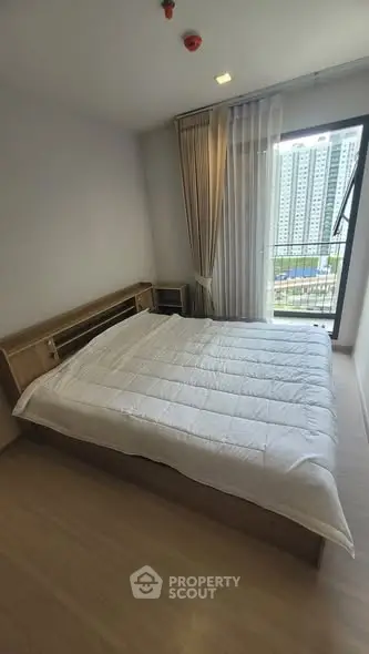 Modern bedroom with large window and city view, featuring a cozy bed and elegant curtains.