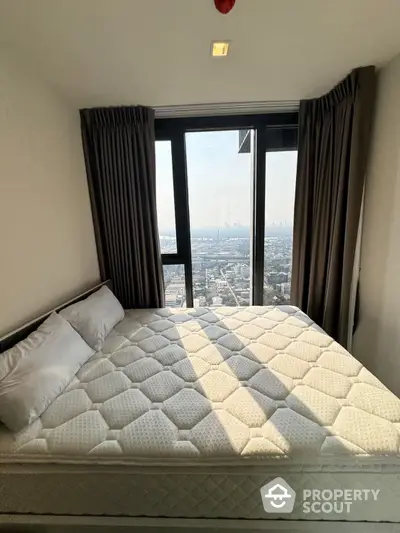 Cozy bedroom with a plush bed and floor-to-ceiling windows offering a panoramic city view, ideal for urban living.