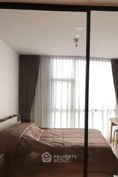 Modern bedroom with large window and elegant curtains, featuring a cozy bed and stylish decor.