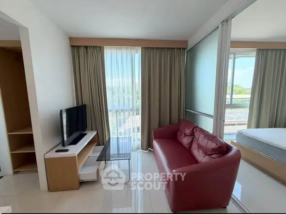Modern living room with red sofa and TV, bright natural light from large window.