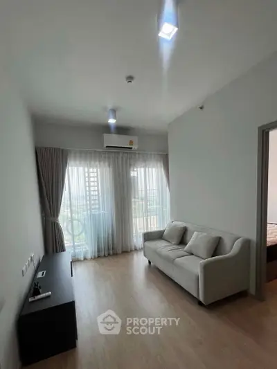 Modern living room with sleek sofa and large window offering natural light and city view.
