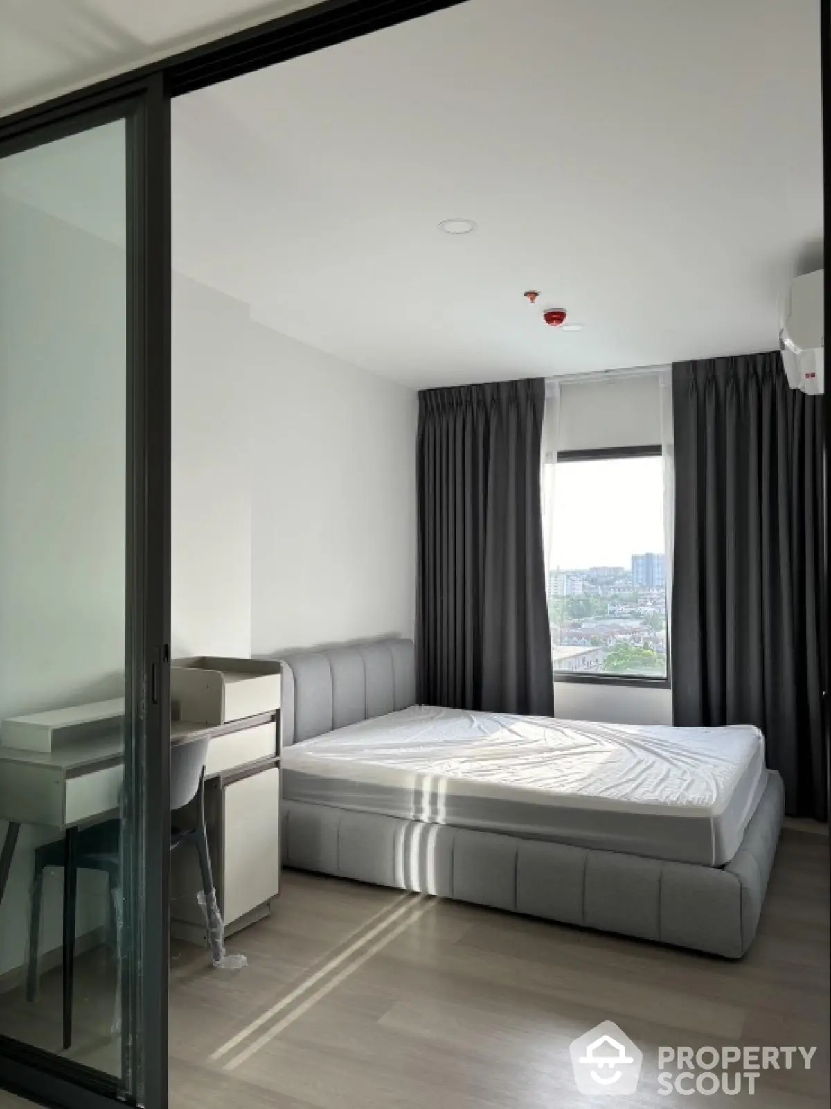 Modern bedroom with large window and city view, featuring a sleek bed and study desk.