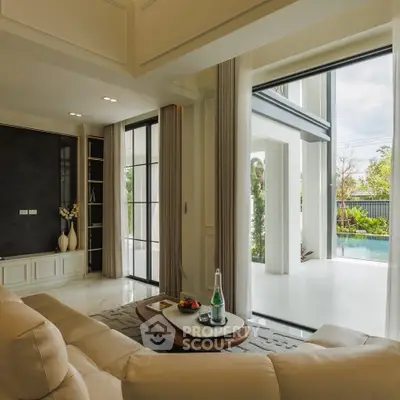 Luxurious living room with large windows overlooking a serene pool and garden, featuring elegant decor and natural light.