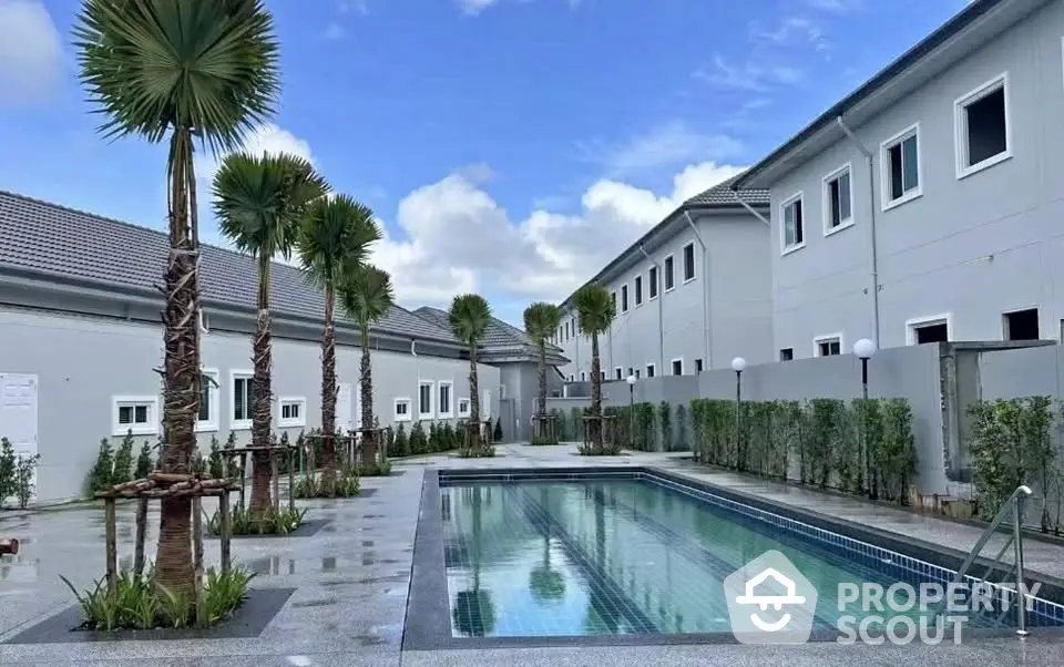 Modern residential complex with a sleek swimming pool and lush landscaping under a clear blue sky.