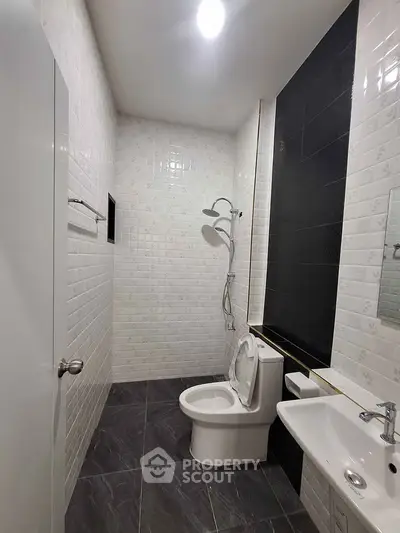 Modern bathroom with sleek black and white tiles, featuring a shower and toilet.