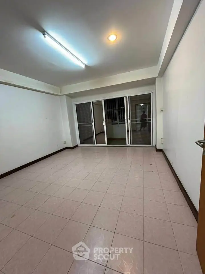 Spacious empty living room with tiled flooring and large sliding glass doors leading to a balcony.