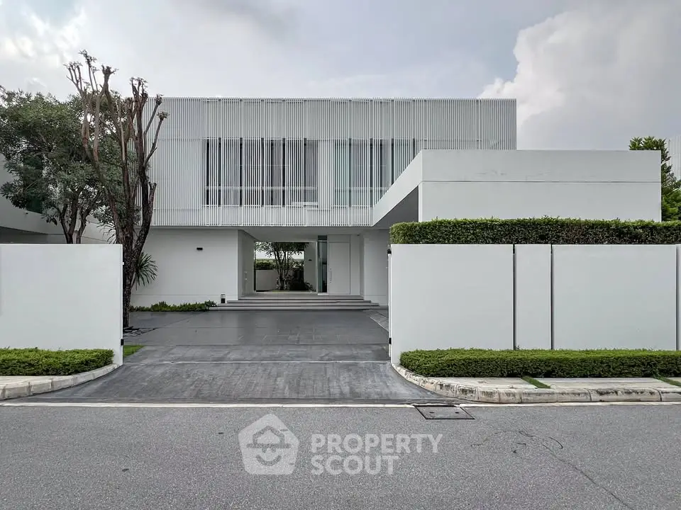 Modern minimalist white house with sleek lines and lush greenery, showcasing contemporary architecture.