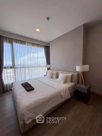 Spacious bedroom with large windows offering stunning city views, modern decor, and ample natural light.