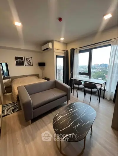 Modern studio apartment with stylish decor and city view, featuring a cozy living area and large windows.