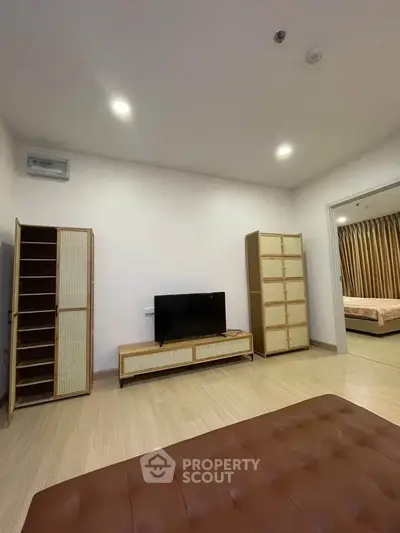 Spacious living room with modern furniture and TV, adjacent to a cozy bedroom.