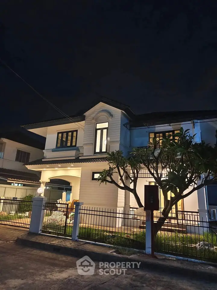Stunning two-story house with elegant facade and lush garden, beautifully illuminated at night.