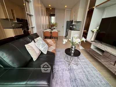 Modern living room with sleek black leather sofa, stylish decor, and open kitchen layout in a contemporary apartment.