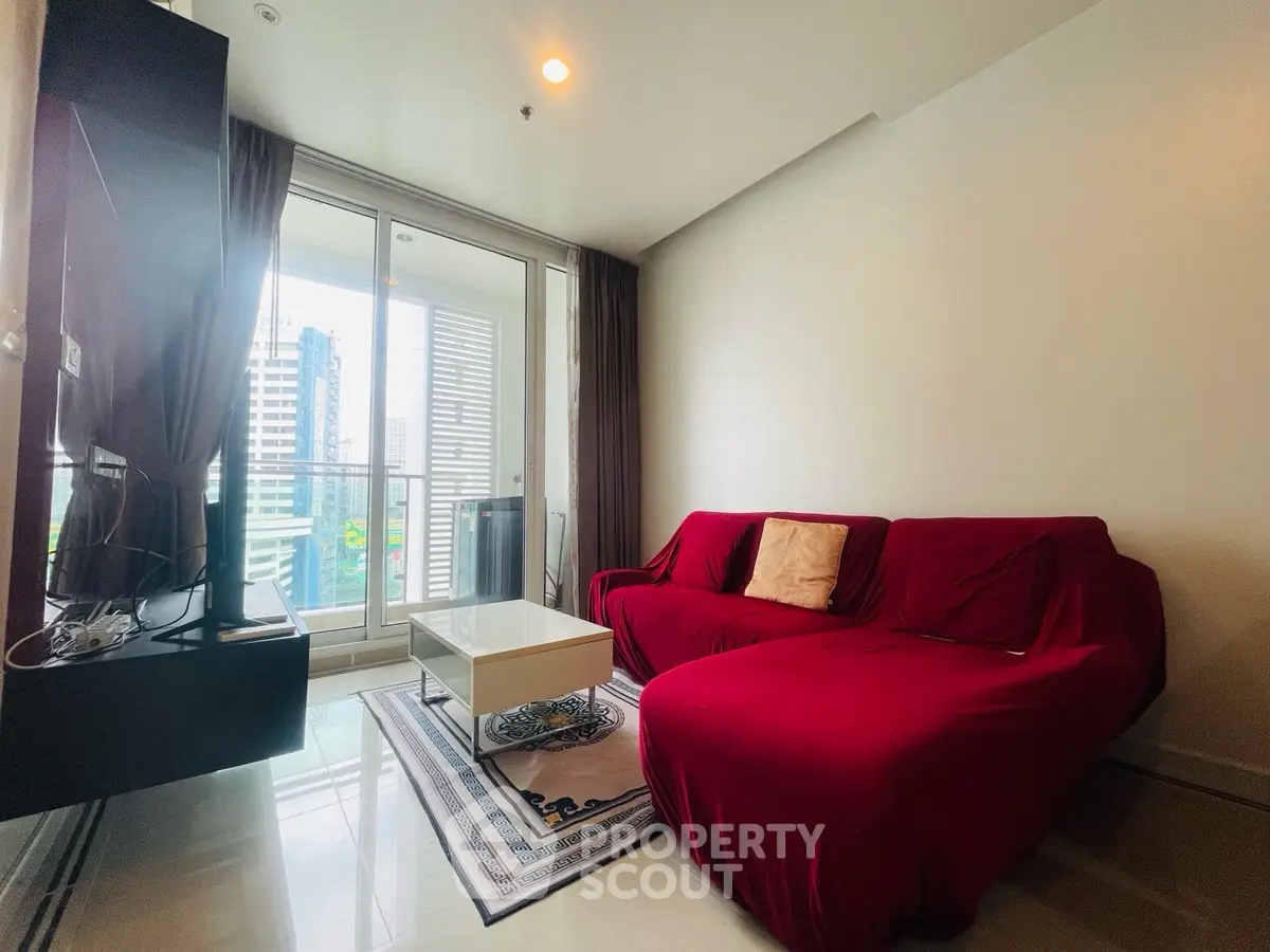 Modern living room with red sofa and city view balcony in high-rise apartment.