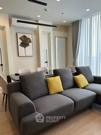 Modern living room with stylish gray sofa, yellow cushions, and elegant dining area in a bright apartment.