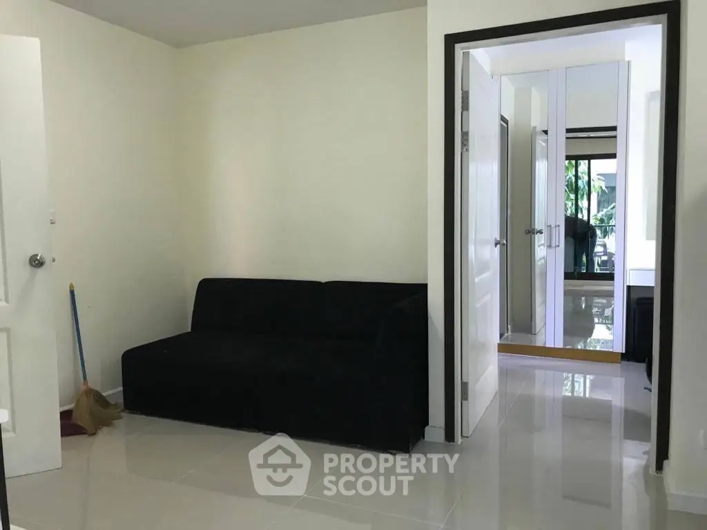 Modern living room with sleek black sofa and glossy tiled floor, leading to a bright hallway.