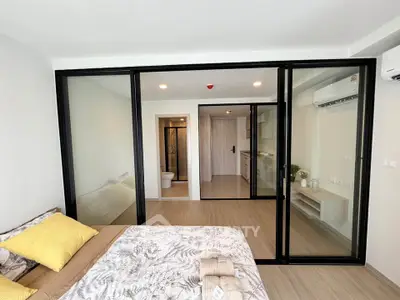 Modern studio apartment with glass partition, cozy bedroom, and sleek kitchen area.