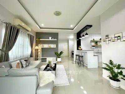 Modern living room with open kitchen, sleek decor and ample natural light.