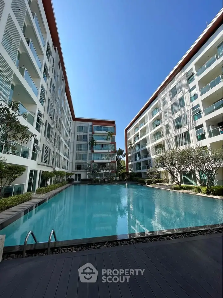 Modern apartment complex with a stunning pool and lush greenery under a clear blue sky.
