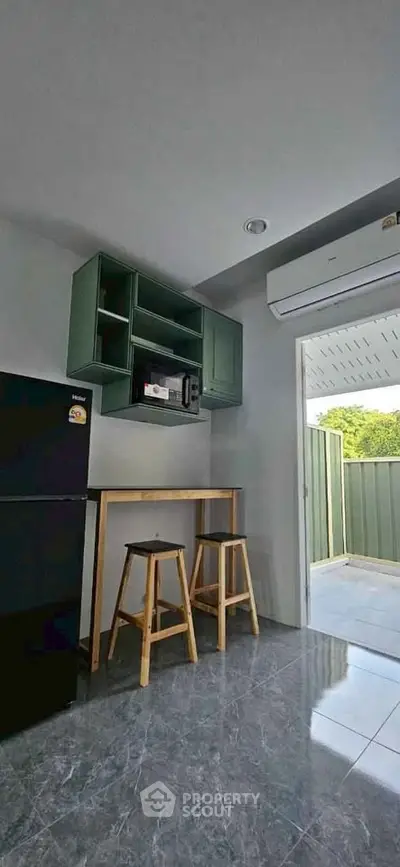 Modern kitchen with green cabinets, black fridge, and outdoor view, featuring sleek design and natural light.